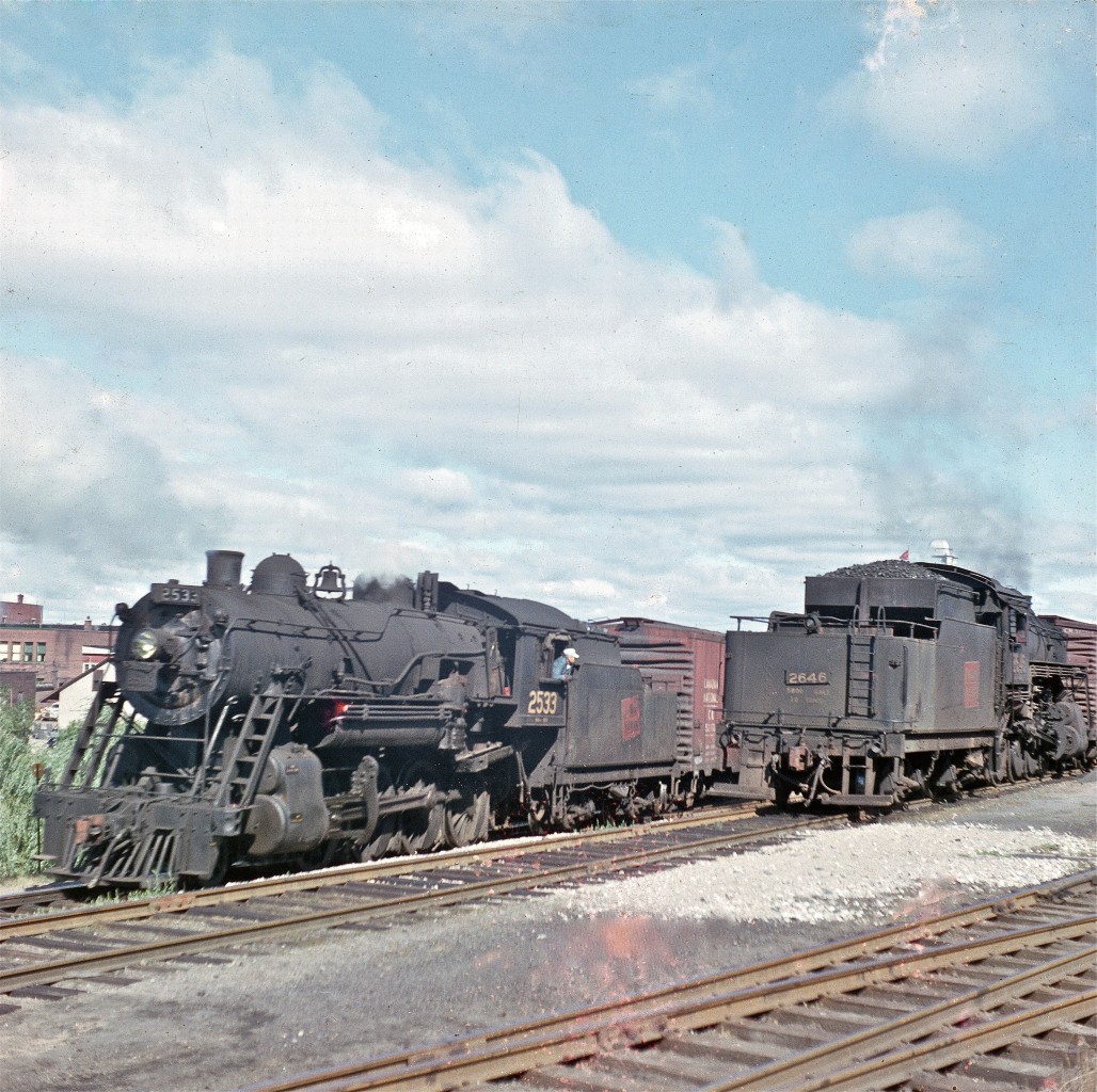 A couple of Consolidation-types work near downtown Pembroke, circa 1959.  Both of these 2-8-0 locomotives were built by MLW.  #2533 was built in 1906, while sister #2646 arrived two years later.  Their days were certainly numbered when Del captured this image.