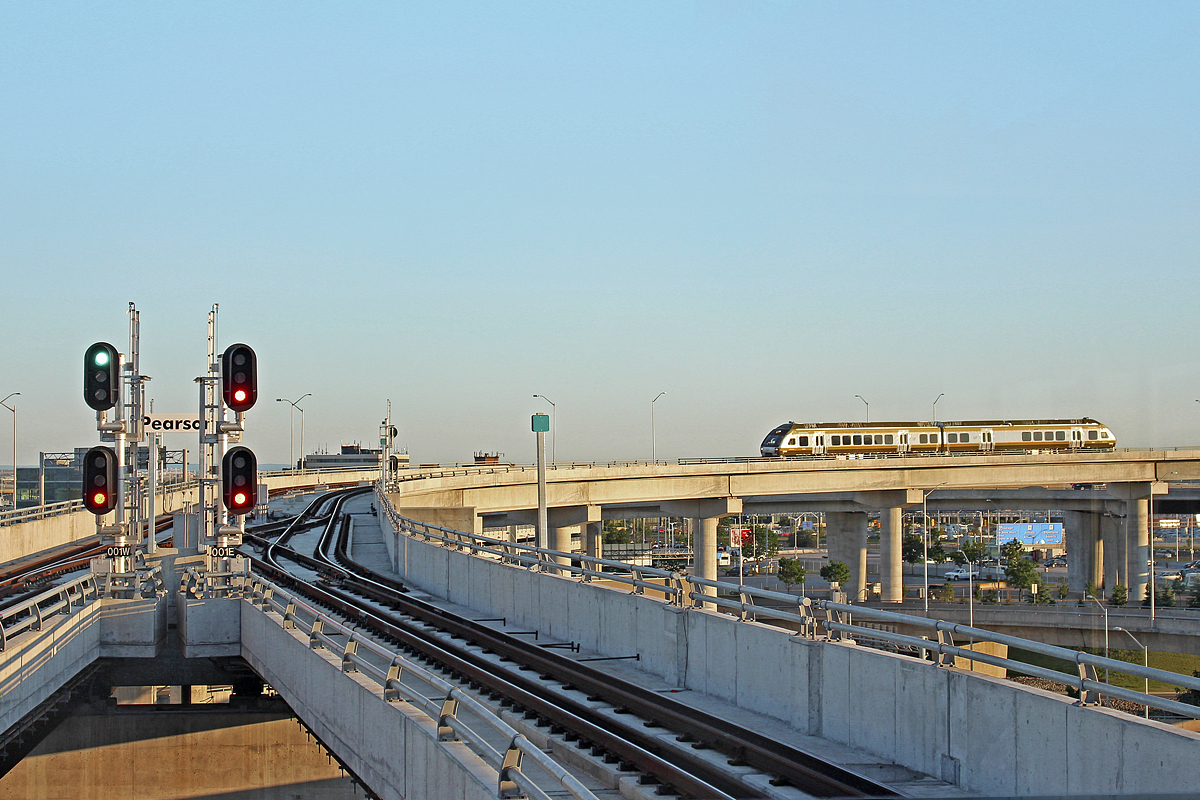 Today is the 71st anniversary of D-day. However, it also marks the opening of the Union-Pearson Express. Construction of this airport-city connection service started four years ago as part of an agreement to host the Pan Am Games. This four year project was by no means a highball. Residents of Weston also put up a lengthy fight to make the UP Express electrified, referring to Diesel Multiple Units as "dirty diesels." They didn't get their way with that, however their concern of the area being divided by frequently passing trains was met with grade separation of all level crossings from Strachan Avenue up to Church Street, costing hundreds of millions. The history of this project lasts far longer than four years, however, and dates back well into the 20th century. While more familiar attempts to start this project began in the late 80s, my papa, who is a baby boomer, remembers from his childhood being told by his dad a train to the airport would soon be built from stories in the newspaper. This story dates back almost sixty years, and my papa, having been let down by many transit projects through the years, was sure it would never be built until he was long gone. Well... my friend, the government didn't let you down this time. 

In direct relation to the actual photo however, here the the third revenue service westbound airport run begins to grind around the last curve before the Pearson interlocking and station. The interlocking resembles a traditional TTC subway crossover, while the signals are very much those found on many mainlines in North America today. The high green is for a train behind me that is almost ready to take off to Union. Mind you, this service will be running every 15-20 minutes. Now Metrolinx... Let's keep moving forward with these badly needed transit projects, such as 2-Way All Day service on every GO train line. Hopefully we don't need another olympic sport event in order for that to happen, as I sure don't think that will happen anytime soon.