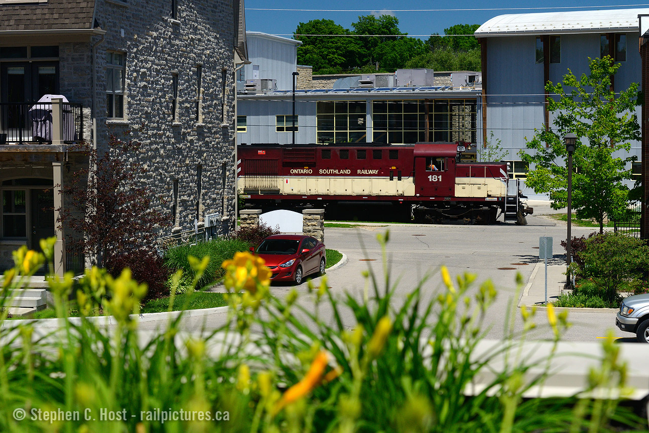 Peekaboo: OSR's only active RS18 (at present) 181 with 505 (MLW RS23) is passing by the Guelph Youth Music Centre, and the Stewart Lofts and Condos in Guelph, both which straddle Cardigan St along with the Railway. Would you live here? Lots of condos currently for sale :)
40 years ago, both CN and CP had tracks here, CP had a piggyback ramp, an interchange, and a CP station was just at the end of the street - along with the usual assortment of switcher engines for local assignments.
And where I'm standing? It was a factory, the former Stewart Planing Mills (Lumber processing).

Photo notes: used a polarizer filter at full blast, shot at 70mm, and higher than usual ISO to account for the reduction in light caused by filter, to achieve a shutter speed of 1/800.