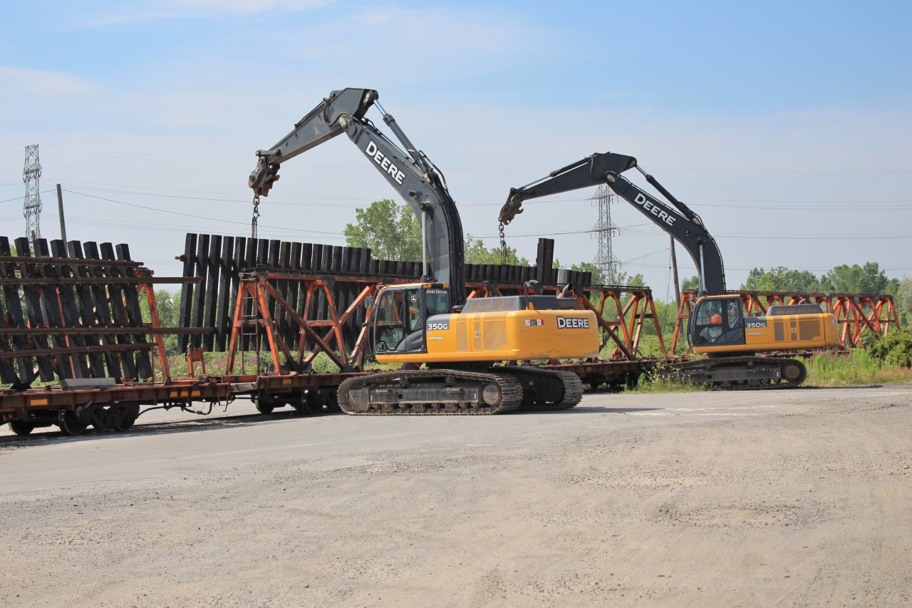 Two large John Deere 350G loaders lift a large section of prefabricated track section off a rail car on the siding at MM32.2 on the CN Oakville sub. They lifted the section up and the truck crew moved the rail car out of position so they could move the section to its destination behind them.