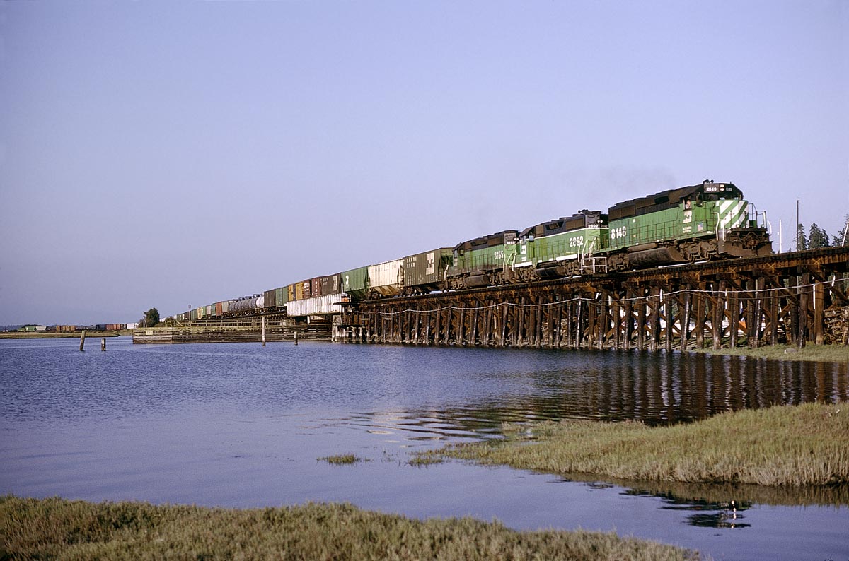 The daily southbound mixed freight crossing the Nikomekl River in the small town of Crescent Beach, BC in August 1993.  There was typically only one daily freight in and out of Canada at that time.  On one of my business trips to NW Washington, I happened to be redirected to the Vancouver airport instead of Seattle and saw this trestle and the one just to the north over the Serpentine River out the window.  I made a mental note to check them out if there was ever an opportunity to be there when there would be a train.  I got that chance on a later trip.  I remember being worried about how slow the train was going and the rising tide, but was willing to get a little wet.