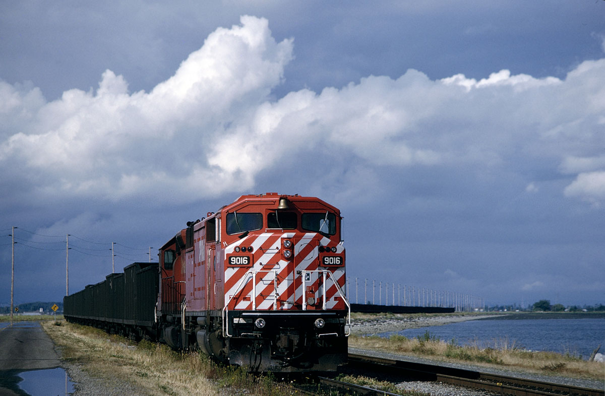 CP #9016 sits waiting for a turn to unload at the Roberts Bank terminal in July 1993.  I had ridden behind the Royal Hudson to Squamish on what had been a very wet afternoon through those clouds in the background of this scene. But when the sun popped out driving back toward the States, I decided that the only chance to find anything in that area to take advantage of the clearing skies would be if there was a coal train staged at the port waiting to unload.  I was rewarded with this CP SD40-2F red barn sitting perfectly in the evening sunshine.
