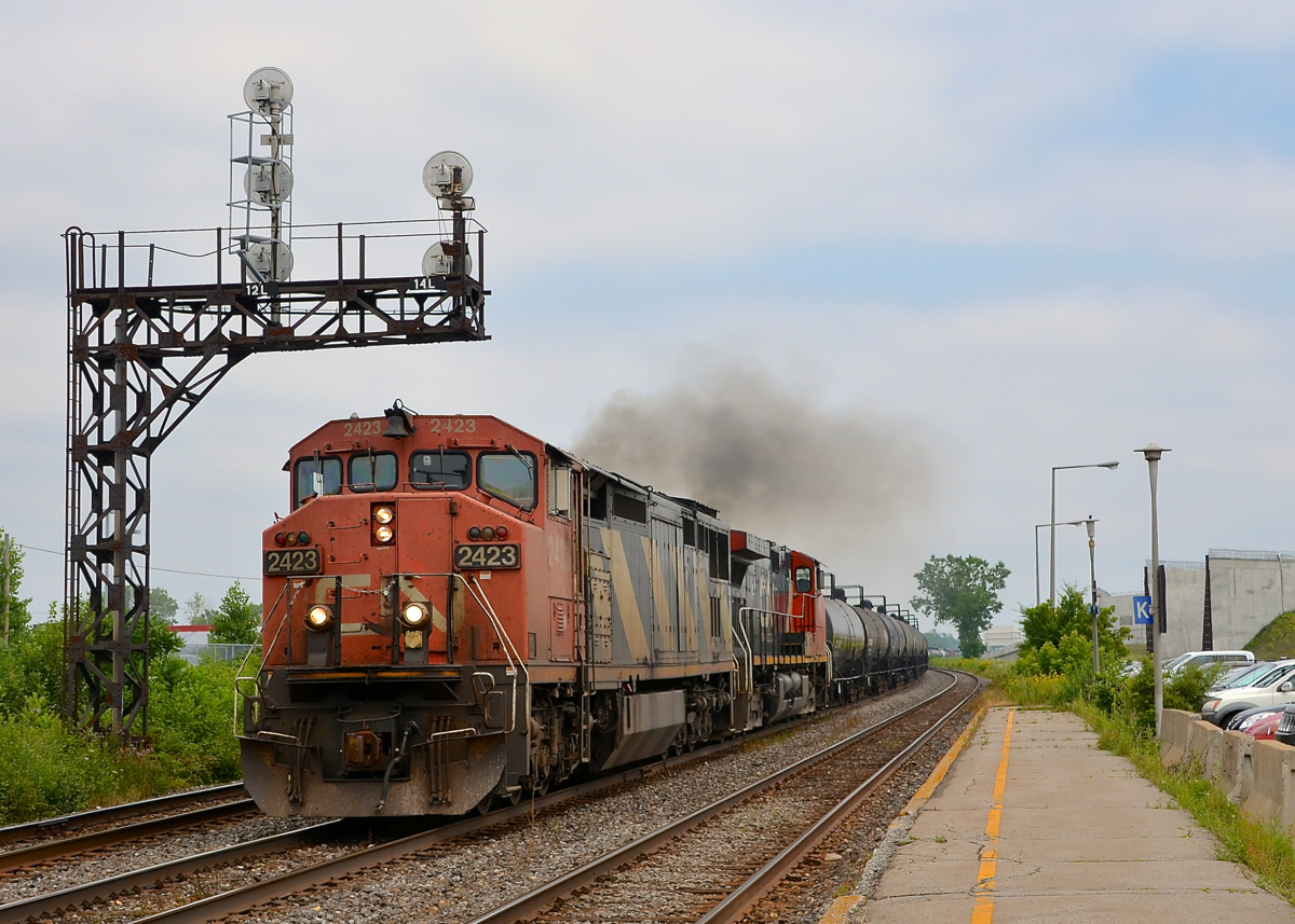 CN 377 passes a signal gantry at Dorval with CN 2423 and CN 2688 as power, both smoking it up as the train accelerates.