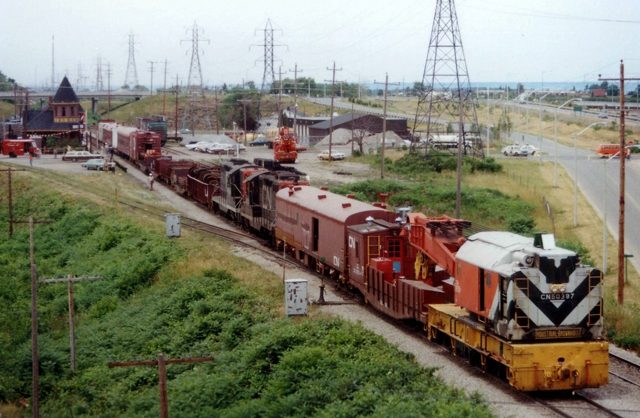 The CN made news for themselves around the Golden Horseshoe back in 1978. Three nasty wrecks within a few months. One at Grimsby preceded another biggie at Stoney Creek by 9 weeks.  At Grimsby, 29 cars of 76 on a westbound #387 hit the skids June 29th just before Maple Av overpass; scattering railcars and blocking both main tracks. This image, taken looking west off that same overpass, shows the CN worktrain on the scene, rolling up to the Grimsby Station. (The derailment a few hundred yards to the east of this image) CN geeps in consist are 4520 and 4509. The station had just undergone renovations and now earned its keep as "Village Depot", a cluster of freight cars posed as "shops" as well as a Keystone Kellys restaurant in the main building. A shoo-fly track is occupied opposite the station, and on the left is the offload track that used to service the old GTR station & other industry many years ago. The GTR station, just out of view, is one of the oldest in Canada and functions now as a Pottery & Antique business.