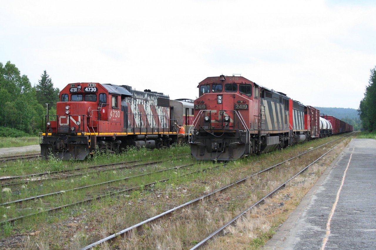 Side by side at Hawk Junction.

CN L571 with CN 2419 in the lead idles in the yard while beside it on another yard track CN 4730 prepares to move the regular passenger train from its overnight storage location over to the station platform.

Officially, the passenger train is a Sault Ste. Marie to Hearst schedule, however since new operator RailMark Canada took full control of the operation in late June, the schedule has been abysmally shattered.  Due to a gross lack of crew manpower, for the last several weeks of operation the train was operating north of Hawk Junction only, if it operated at all (an investigation into allegations of a major rules violation at one point shut down service for almost an entire week, stranding passengers and giving RailMark a huge black eye; the crew was apparently later cleared of wrongdoing, but could not operate a train during the investigation period). 

Sadly, the train seen here is actually the last northbound run of the passenger train out of Hawk Junction, as CN had put a stop to their relationship with RailMark effective July 15, 2015. And this train would only operate as far as Oba to runaround and return to Hawk Junction later that evening, with the equipment shipped off to Sault Ste. Marie the next day for storage.