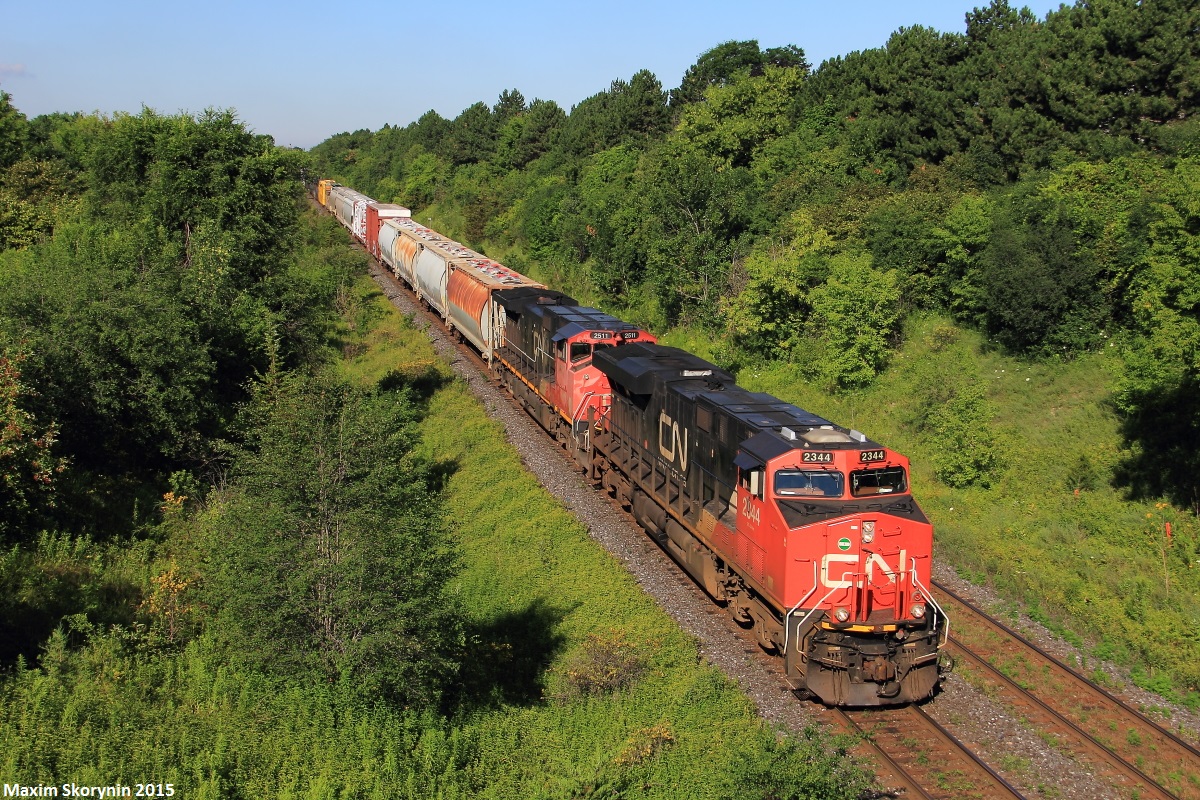 A ES44DC and a DASH 9-44CW are on point of this day's M37231 train with a SD70M-2 locomotive pushing mid-train, en-route to Montreal from Toronto. Yesterday on July 18th of 2015, train Q14921, Montreal - Chicago train derailed on the Kingston Subdivision just east of Oshawa in Bowmanville, with 7 cars propped off the track. No injuries were reported, however this stopped all other trains on the line. The next day when all was cleared up, all the trains that were supposed to be pass by yesterday are now adding up and passing today, including the train in this picture, which is usually seen around the area at about 4-5pm, making this an extremely rare catch in good light.