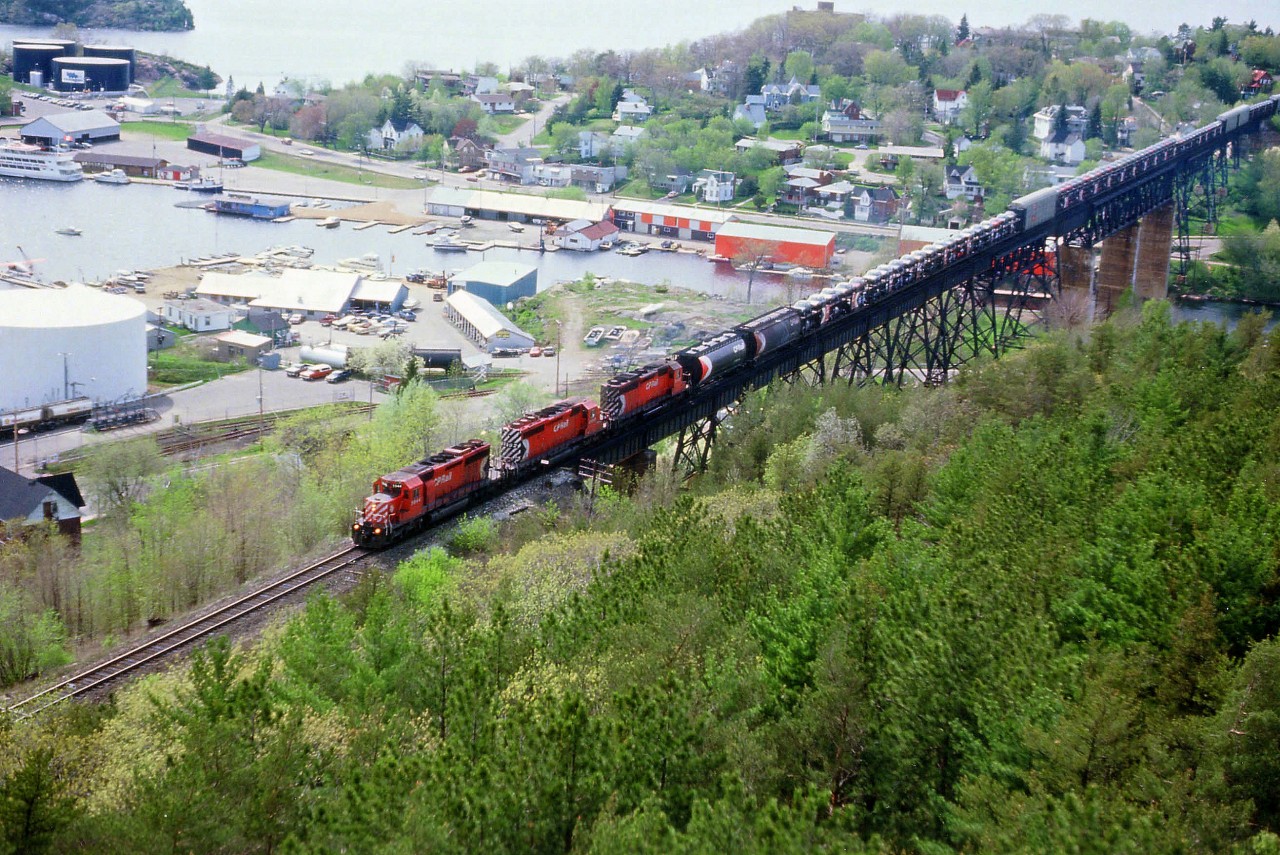 The sun is high overhead, but then, so am I, as I capture a nice shot of a southbound CP en route to MacTier for crew change, then onward to Toronto.  The view from the Fire Tower at the park is always worth checking out, but these days the forest of evergreens has reached the height that affects a clear shot of trains running south of the bridge. Also, directional running here now has most all trains operating as Northbounds on this CP and Southbound on the CN thru town. So, this shot now would be considered a rare catch. A long string of open autorack cars behind something like CP 5944, 5992 and 5547 is certainly a sighting of the past. Note to the left of the lead unit one can see the CN industrial trackage as well; which served the storage tanks. All of those are gone, as is the track. At 1,700 ft in length, the bridge over the Seguin River in town is a "must see" for those who have not yet been there.