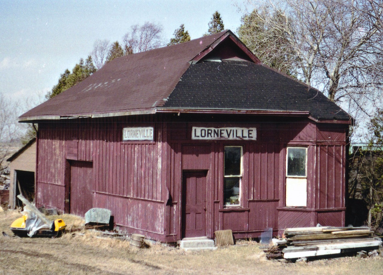 A decent early spring day on my day off work and once again I grabbed the little woman sidekick by the arm and hauled her off on another one of my wild goose chases. Looking for railroad stations I had heard were still in existence. Time was running short. These buildings in the mid to late '70s were coming down like dominos; having outlived their usefulness and becoming an annoyance for the railroads. This trip took us to check out Richmond Hill for the ONR-CN passenger at 0720, to Bradford, Barrie, Shanty Bay, the Orillia station and Trolley #4 as well as Gravenhurst and Washago. On the way back, we were to follow the roads to the east side of Lake Simcoe, specifically to check out "Elmer Jordan's farm, somewhere along old Ontario Hwy 46, location now I have forgotten, but somewhere near Woodville, call that just east of Cannington. This wasn't going to be easy, I thought. But, stopping at a general store in the area, I was told exactly how to get to Elmer's place; I guess he was well-known, and we made it there with little trouble. Now I wish I had made note of the directions. He was quite the friendly old guy (It helps to have a female with you) and sure enough, this little station was out back, hidden from view by a rickety old barn and a pile of typical barnyard junk. I loved it. Still had solid floors, the pot-bellied stove, and the whole bit. Apparently Elmer in his day used to work for the railroads, and when this station became expendable, he bought it and moved it to his farm. The building, a historical big deal to me, is the very last artifact out there from the early Toronto & Nipissing Rwy. It was at the junction of the Midland Rwy just north of Woodville; official name was Lorneville Junction station and it was a beehive of activity for people going from east/west and north/south here. Toronto to Coboconk or Beaverton to Lindsay. It has been 38 yrs as of this writing since I have seen this building. Now, as I write this caption,  I get to wondering what has become of it. Has it collapsed and died like so many farm outbuildings have over the past years? It is worthy now of a trip back, I should think.  Soon. It may already be too late.