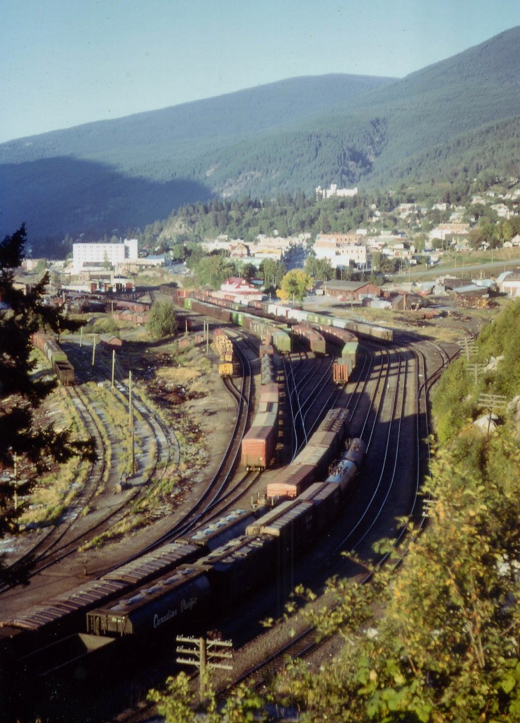 If there was a "time machine" update from this location, I'd sure like to see it. Out in the BC interior I was on vacation with the girlfriend, staying at my grandfathers home in Boswell, about 30 miles away, other side of the water. We headed out for the day; she in anticipation of somewhere 'exciting', but no, she forgot there were train yards in Nelson.........  This view I found along Hwy 6 at the west end of town; and I wonder if this location is still as open today.  The image was taken late afternoon; and visible dead center is the old Nelson CP station, built in 1900 and after passenger service ended deteriorated to the point it was a wonder vandals didn't torch it. In 1992 it was declared a Heritage Building and I understand it has been restored. On the left barely visible is the famous Nelson Diesel Shop, built 1953, home for the CLC locomotives in the west; after their demise the shop was closed, and what was declared an 'eyesore' was torn down a few years ago. (2010?) This was quite the facility in its' day.  Note the string of cabooses (cabeese?) I'd love to know what is left of the facility here.