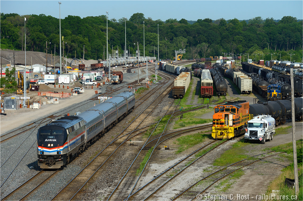 Can you spot all four trains? As you can see in this photo, the plant at "stuart" is fully in service, GO trains are in fact going in and out of here nearly daily (Training? Testing? Revenue service has yet to begin..) Metrolinx announced the start of service for Thursday July 9. For those who don't live here - the Greater Toronto area is preparing for the Pan-Am Games which start in the next couple weeks and this is partially why some of these massive projects are occurring now - Union Pearson Express, this station, and much more. In particular, the platform for the station behind me is still unfinished and the station only 40% complete at best, and yet, in 6 days, service starts.... I am actually looking forward to being able to take advantage of the platform once service begins - should open up a couple different angles here 
So back to the photo at hand - I count myself lucky - a side by side is hard to get - 3049 was busy switching cars in the yard, ducking in and out at right for the 30 minutes leading up to 97's arrival.  Will I get a side by side? Just before Amtrak was to come, the fuel truck pulls up beside 3049 and the crew took the break while the engine was refuling. Count my lucky stars.. I seem to have a few lately. :) 
So as I asked - where's Waldo? Or better yet, post in comment where the other trains are. :)