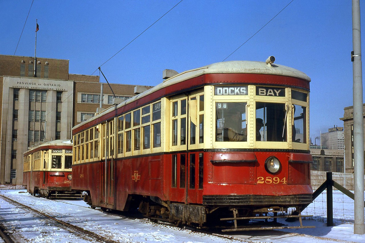 Toronto Transit Commission Peter Witt streetcars 2894 and 2834 sit at Ferry Loop off Queen's Quay, signed up as Bay and Dupont cars respectively, but both destined for the Docks (here). The TTC's Peter Witt fleet was running borrowed time, with only a few years left before the remaining cars were retired from regular service at the beginning of 1965. Ferry Loop, built in 1961 due to route changes associated with the Gardiner Expressway, would also stop being used in September 1965. In the background is the Government of Ontario Workmans Compensation Board building in background on Harbour Street (built 1953, later became the OPP Headquarters, demolished 2011).  Both cars were part of the 2800-2898 group of "small" Peter Witt cars (only even numbers) built by the Ottawa Car Company in the early 1920's. Car 2834 was likely scrapped sometime after retirement, but 2894 was sold off and sat in a barn on a property near Barrie, before the TTC acquired it back for overhaul and use on the Belt Line Tour Tram service in the 1970's. Today it resides at the Halton County Radial Railway Museum offering rides to visitors.  TTC 2834 and PCC car 4518, at Ferry Loop on the same day: http://www.railpictures.ca/?attachment_id=19019