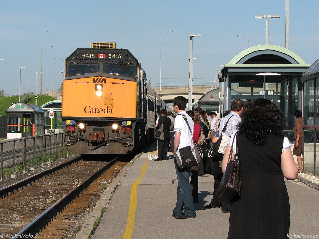Brampton commuters clutching their morning coffees, daily newspapers, bags and other belongings await the arrival of GO Transit train #210, the 8:10 from Bramalea to Union, to head into downtown Toronto for another workday. Like clockwork every morning, VIA #86 with bright yellow-nosed F40PH-2D 6415 on the head end rushes past non-stop for Toronto, running ahead of GO #210 and having made its final stop in downtown Brampton minutes ago.