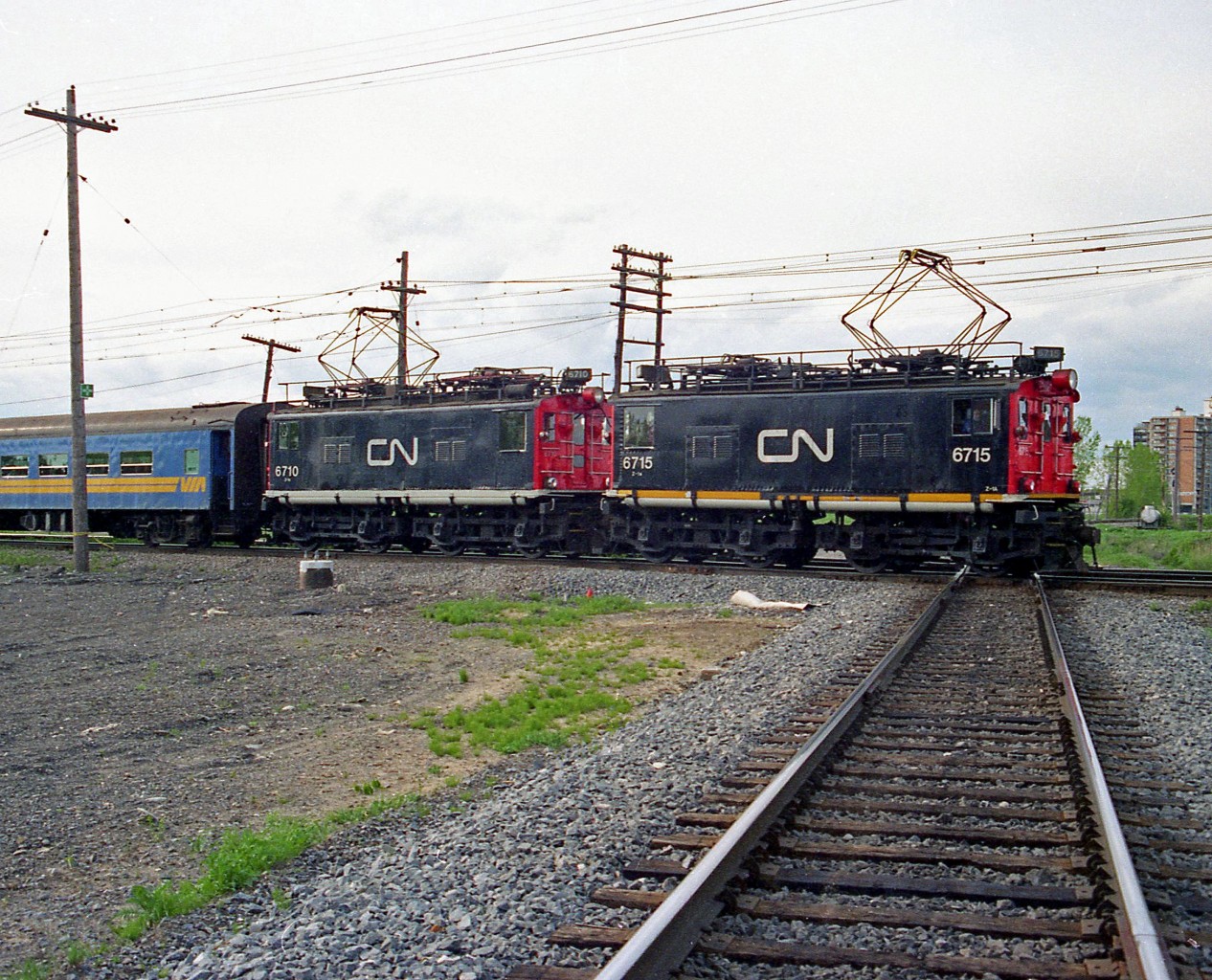 CN Z1a-class GE boxcab electric locomotives 6715 and 6710 (built 1916 and 1914 respectively) handle a commuter train with VIA-painted coaches, crossing the diamond with the CN St. Laurent Subdivision at Eastern Junction in May 1995. It was all but over for CN's vintage electric fleet still employed in Deux-Montagnes commuter service, as the remaining units retired a few months later when the final phase of renovations were completed on the line in Summer/Fall 1995.

Lead unit 6715 is preserved at the National Museum of Science and Technology in Ottawa, while 6710 can be found on display in front of AMT's Deux-Montagnes station.