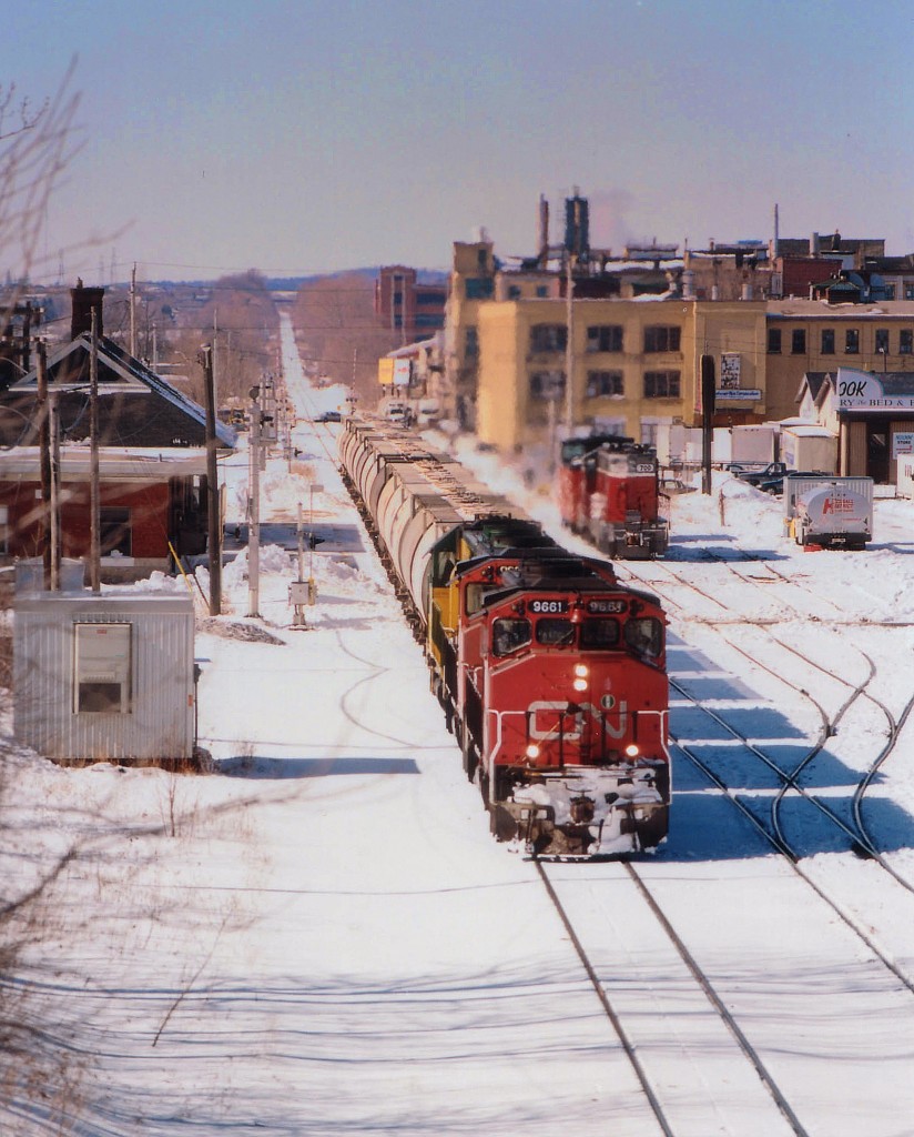 The GEXR takeover of the Guelph Sub was in its' infancy at 5 months when this shot was taken; and the railroad was forced to lease CN locomotives in order to cover all bases. Here we see from the Margaret Av overpass the eastbound morning GEXR #432 as it passes the Kitchener VIA station. Power is a couple of leased CNs, 9661 and 9633 with GEXR 4046 trailing. The CNs have long since departed the roster, and the GEXR has been scrapped. The area in this photograph is undergoing massive changes as preparations for GO service is under way.