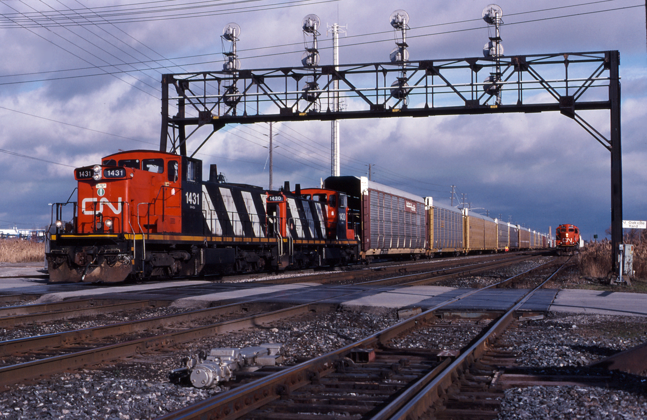 CN 1431 and CN 1430 pull down the yard lead with a cut of racks from the Ford Plant while another road switcher works the south yard, which typically held cars for the many industries along the Oakville Sub.