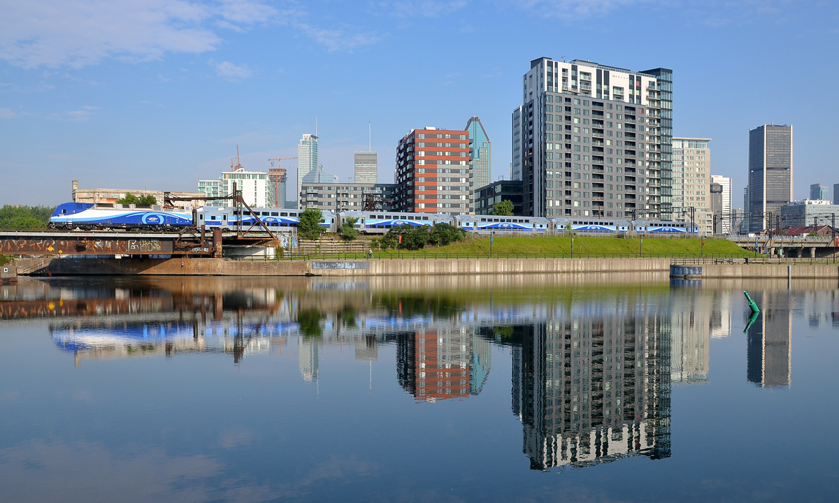 A 100% Bombardier consist reflected AMT 809 with Bombardier ALP-45DP AMT 1350 pushing five Bombardier multilevel cars is reflected in the Peel Basin in Montreal on a very hot morning.