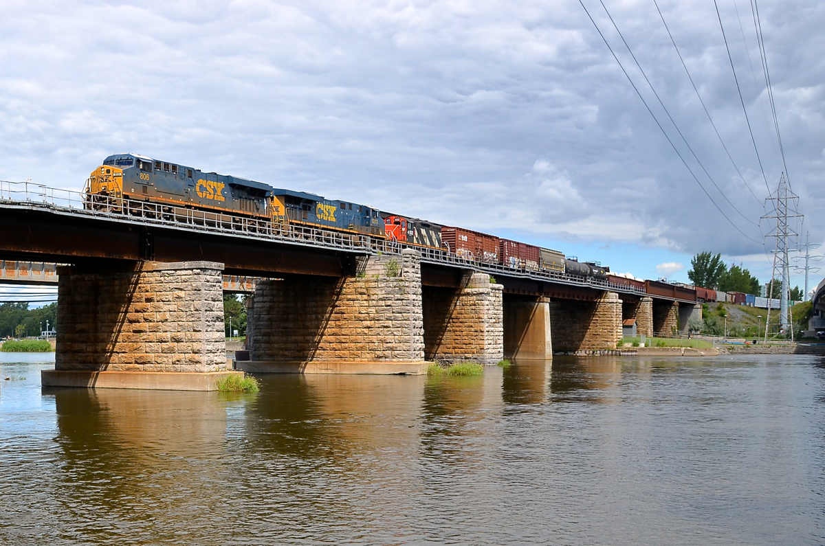Two CSXT GEVO's and a CN GP9. CN 327 has a pair of CSXT GEVO's (ES44AC CSXT 806 with steerable trucks and ES40DC CSXT 5272 with conventional hi-adhesion trucks) and a CN GP9 (CN 4102, which will be set off at Coteau) as it crosses over the Ottawa River during a brief period of sunshine.