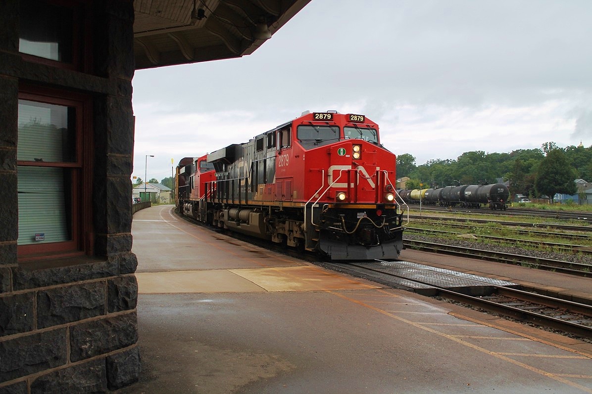 A morning of thunder showers and dark skies greet this eastbound mixed freight as it passes the stone façade of Brantford station. CN 2879 and 2910 apply the power.