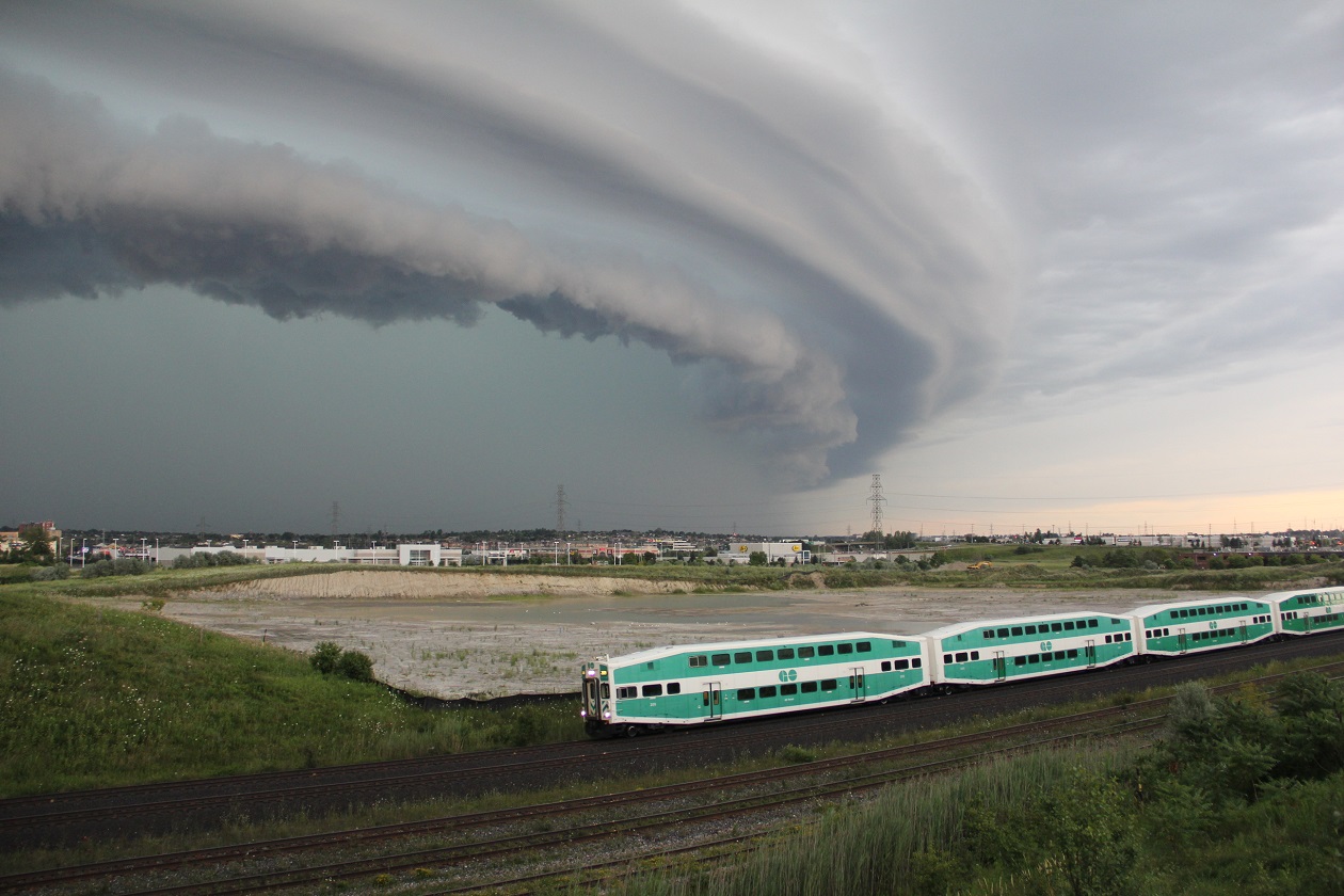 A WB GO train  passes an approaching summers afternoon thunderstorms au minus clouds.