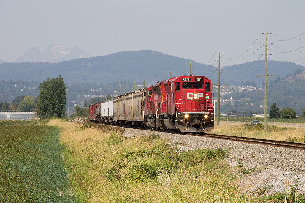 CP Sumas Turn is observed heading southbound just north of the historic Clayburn Diamond, for Huntingdon, BC with a pair of SD30ECOs in charge. Since coal has slowed down, all 20 of these units have been pulled from service and instead are working as transfer power. For this photographer these units make him think CP has designed a modern day SD45. To the left of the image is a hazy Mount Robie Read towering over Mission, BC.