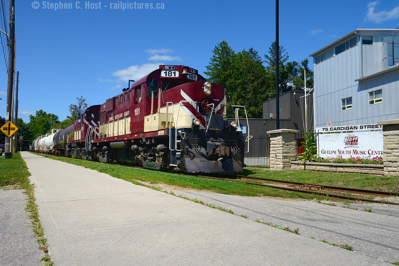 Opposite the sidewalk along Cardigan St, OSR's Monday to Friday Guelph job is southbound heading back to lower yard with 20 cars in tow. At right is the Guelph Youth Music Centre.