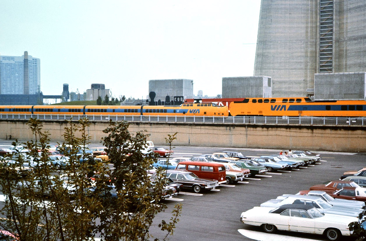 Art is imitating life as a VIA Rail Turbo Train set moves from Toronto Union Station to the Spadina Avenue maintenance facility on an overcast early fall 1976 afternoon.
The painting of a steam engine, diesel locomotive and a Turbo Train once adorned the poured concrete retaining wall at the base of the CN Tower.
The waterfront skyline in the background, and most of the automobiles in the foreground are unrecognizable today. My brand new 1976 Plymouth Road Runner is hiding in the trees at the lower left corner of the photo.
My brand new CN office at 277 Front St. W. along with the Metro Toronto Convention Center are almost a decade away from being completed on the very spot where I took this photo.
Almost 40 years later, the Turbo Train, the wall painting, the Road Runner, and the CN office are all gone.