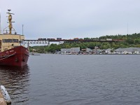 A CN stack train heads over Parry Sound harbor with MV Still Watch still watching. The ship was built in 1960 as a research vessel for the Canadian Coast Guard and is now privately owned.