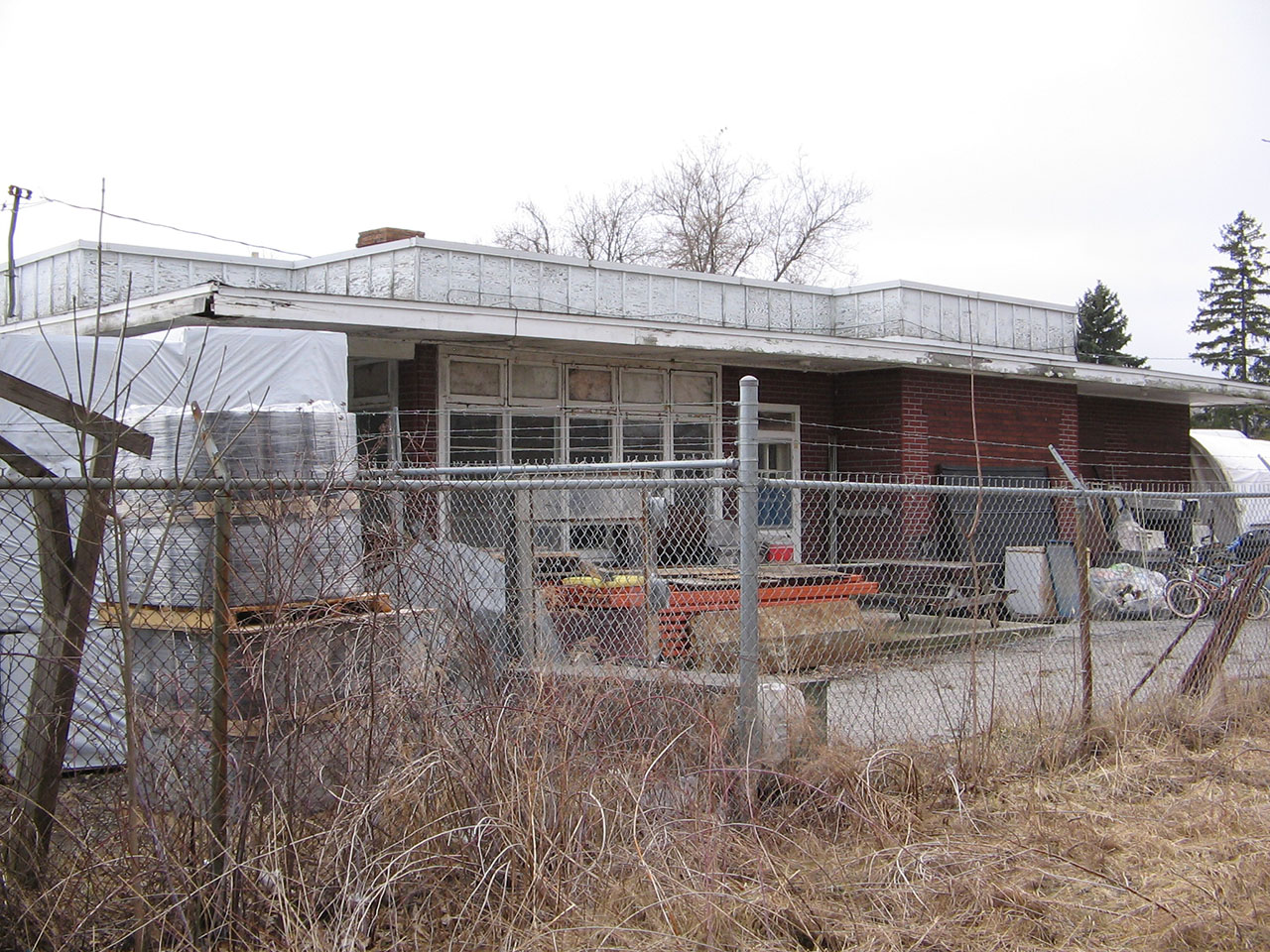 I have had the pleasure to photograph this station only a couple of times. 

The first time, I saw that the owner was on site, walked up and into the station where he and a few of his friends were having a couple of beers - politely introduced myself and asked if I could wlak around and take a few photos of the old station. Before I knew it - he grabbed the hand that was holding the camera - and in a polite way, asked if he could comphiscate my camera! When I politely refused, and explained further why I wanted to photograph the station, he gave me permission and apologized because he thought I was with the Building Commission for Norfolk County. The owner apparently had secret plans to sell the land and the station, to a developer who wanted to demolish the station and build condos overlooking Silver Lake. He didn't want those 'historical preservationists' to know about his plans so that they could fight to save the staton. He limited me to the outskirts of the fence around the station.

This photo was my second time photograhing the building, and I never forgot the owners words. The station still stands, and hasn't been torn down yet.
