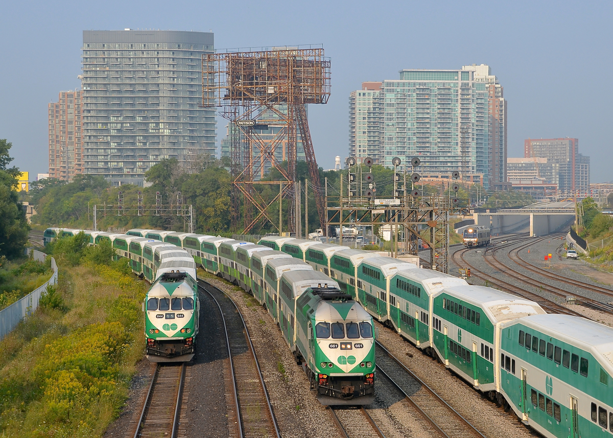 A triple GO meet, with a shuttle approaching. A GO Transit train is inbound, passing stopped trains on either side. In the distance UPX 1001 approaches with a shuttle from Pearson Airport.