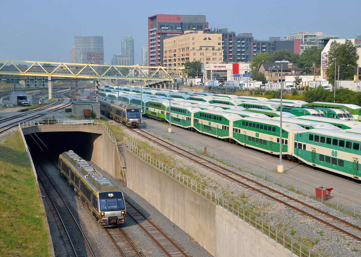 Airport shuttles on two levels. An inbound Union Pearson Express train is below as an outbound train passes above, going from and to Pearson Airport. At right is the GO North Bathurst Yard.