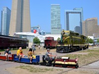 <b>Mini-train passing standard gauge equipment.</b> The Toronto Railway Museum's mini-train passes some preserved equipment, including GP7 CN 4803. In the background at left is the base of the CN tower.