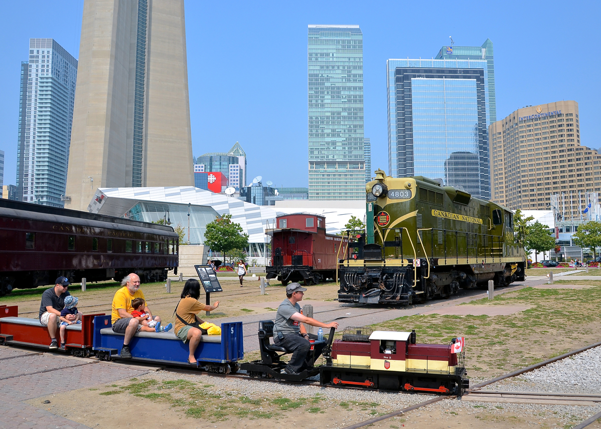 Mini-train passing standard gauge equipment. The Toronto Railway Museum's mini-train passes some preserved equipment, including GP7 CN 4803. In the background at left is the base of the CN tower.