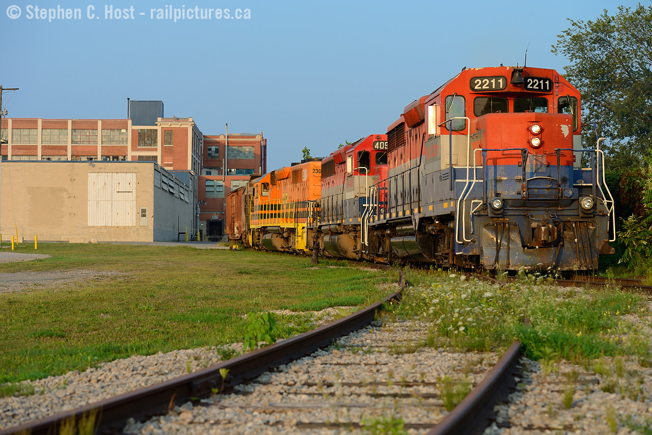 Switching Airboss in Kitchener, the hogger is gingerly guiding his train on track rated for 5 MPH maximum speed. Lifting one car out of the plant door, the hopper is likely an idler. There wasn't a heck of a lot of sunlight left by the time I found this scene..

This shot has taken quite a long time for me to achieve - seeing that Airboss is normally switched either first thing in the morning or late after dark and the light is only good late in the evening. What's neat about this location? The ancient factory - built in 1913 - formerly the  Dominion Tire Plant (click for more) it hasn't really changed much since then. -This is probably one of the oldest factories still receiving somewhat continuous rail service - and to make it even more dramatic -  and this plant is very close to condo development where similar factories have been converted over and continue to be.
Secondly, this plant would have had electric overhead wire for the motors of the Grand River Railway (thusly the CP Waterloo sub). While the electric overhead was removed in 1961 when the GRR dieselised, CP continued to serve this plant likely into 1994.

And one tidbit we locals know - back in 2005 when EMD was going gangbusters pumping out new CSX, UP, and BNSF SD70ACe's the facility behind me where this spur leads to was used to finish SD70Ace's for EMD - never did catch an engine going in or out of here, from what I recall the moves were done very 'hush hush' at the time. A little known fact, mind you.. 

What old factory do you wish you could see a railcar coming in or out of that still has a chance of happening?