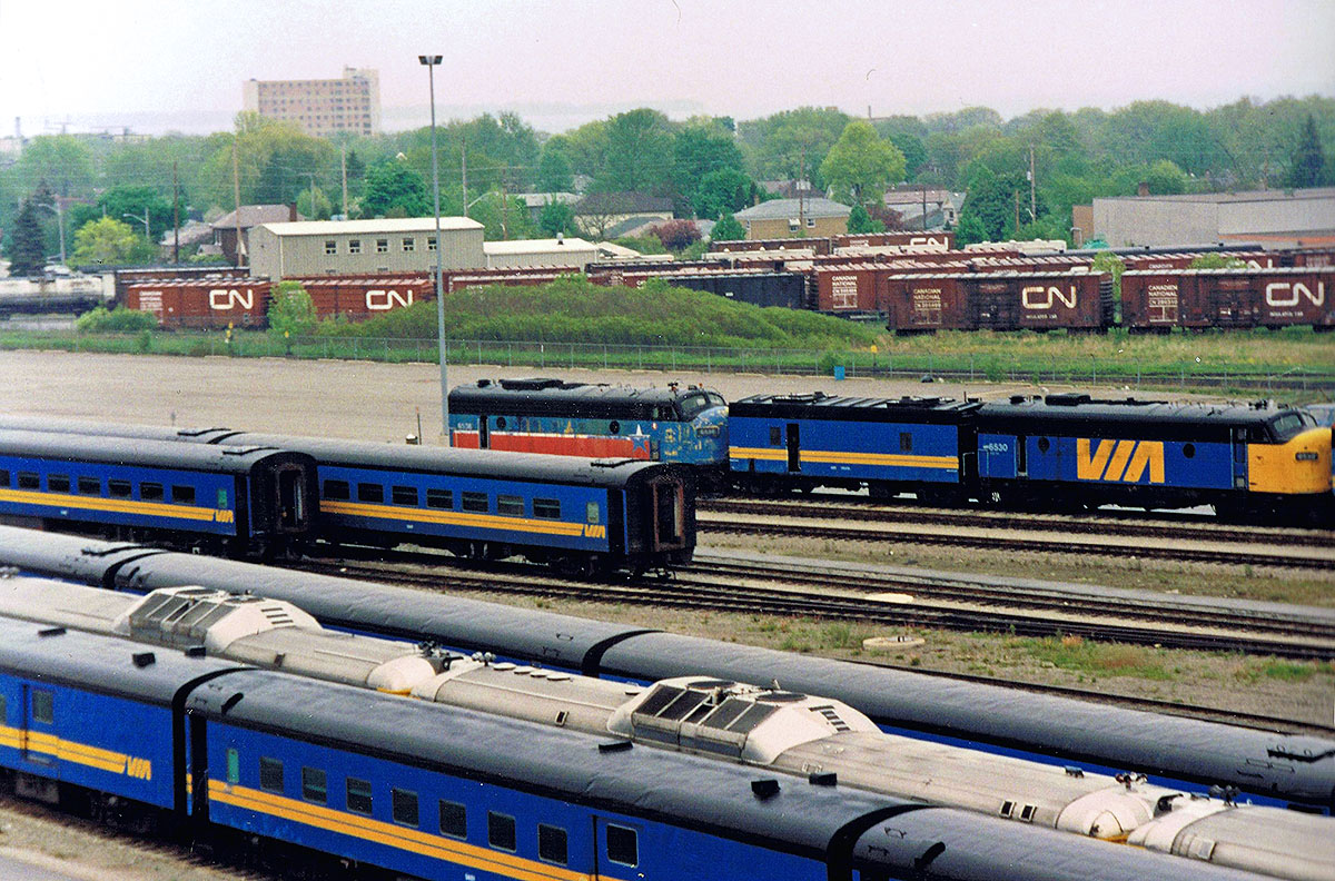 VIA FP9's #6530 & #6536 (in an unusual paint scheme) sandwiching a steam generator car at VIA's Toronto Maintenance Center. In the 1990's the Federal Conservatives enacted a round of draconian funding cuts resulting in a massive reduction of VIA Rail services (and retirement of first generation power). History would repeat itself 2 decades later with another round of cuts under the current Conservative government. Note the large number of CN boxcars in the background, and former CN steam heated passenger cars (including a combine) & RDC's in the foreground. For more pics & videos from my collection see my website at  http://northamericabyrail.info  , Cheers, Pete