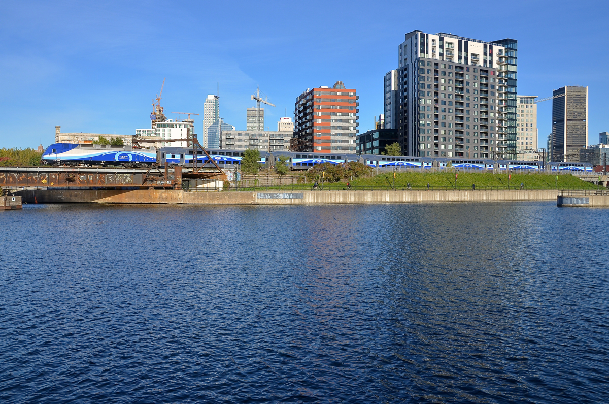 A blue striped train. AMT 809 passes the Peel basin before entering Central Station in Montreal. The blue stripes on the AMT train contrast with the darker blue water in the basin.