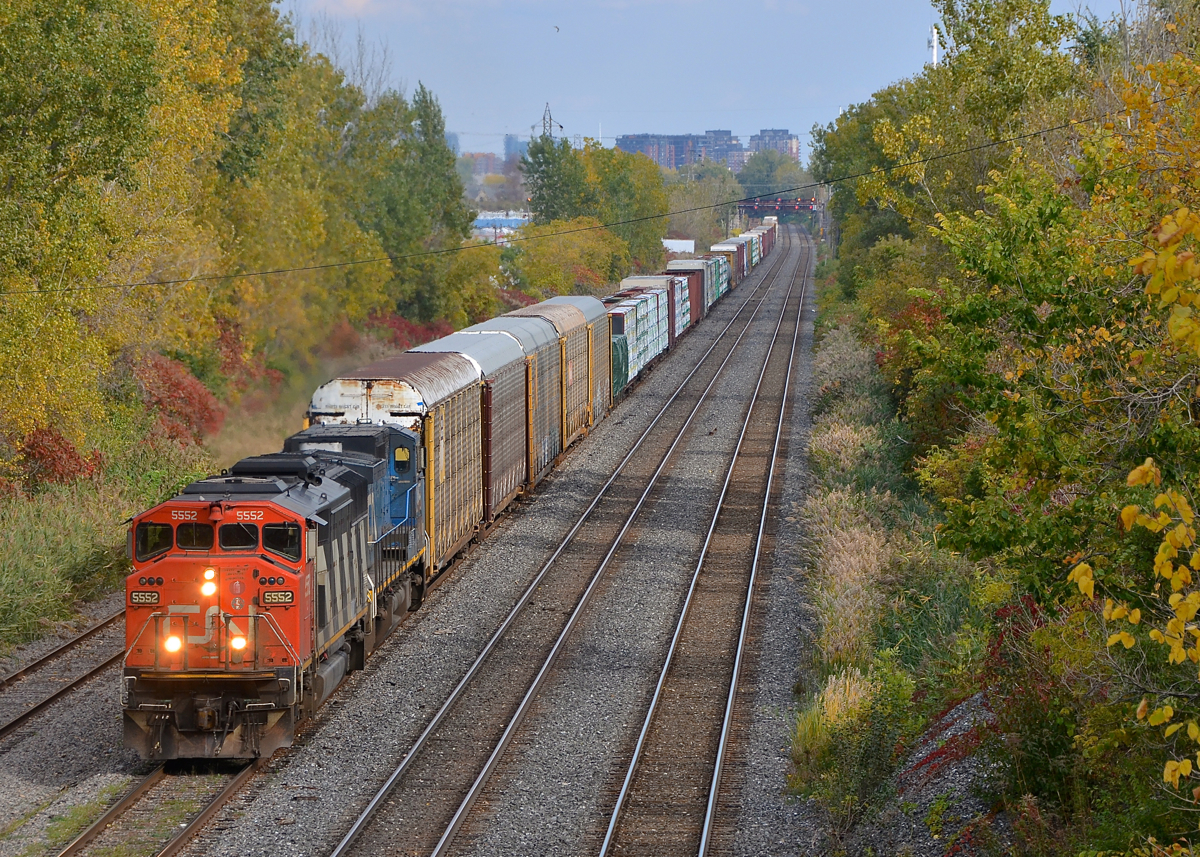 A striped plow on a zebra striped cowl. CN 5552, still sporting its striped plow as delivered, leads CN 401 towards nearby Taschereau yard. Trailing is 'blue devil' IC 2455.