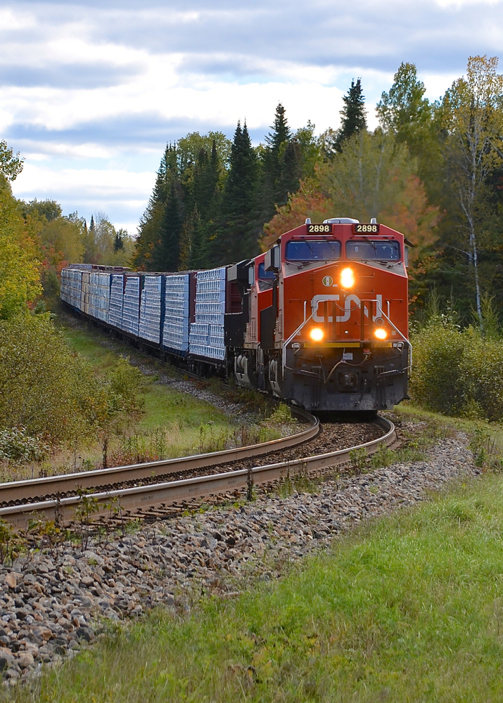 Dropping downhill. The up and down nature of the CN Lac St-Jean sub is graphically illustrated by CN 369 dropping downgrade before curving towards a crossing. Power is 4 AC units: CN 2898 & CN 2949, along with CN 2854 & CN 3000 mid-train.