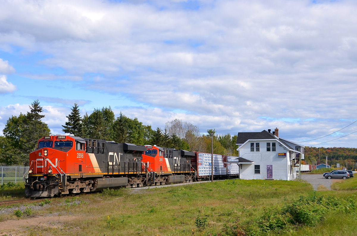 Past Hervey Jct station. CN 369 is passing the Hervey Jct station on its way to Garneau yard. Cars are parked in the parking lot, awaiting the arrival of the combined VIA 601 & 603 which will arrive in about half an hour before splitting up here. Power is 4 AC units: CN 2898 & CN 2949, along with CN 2854 & CN 3000 mid-train.