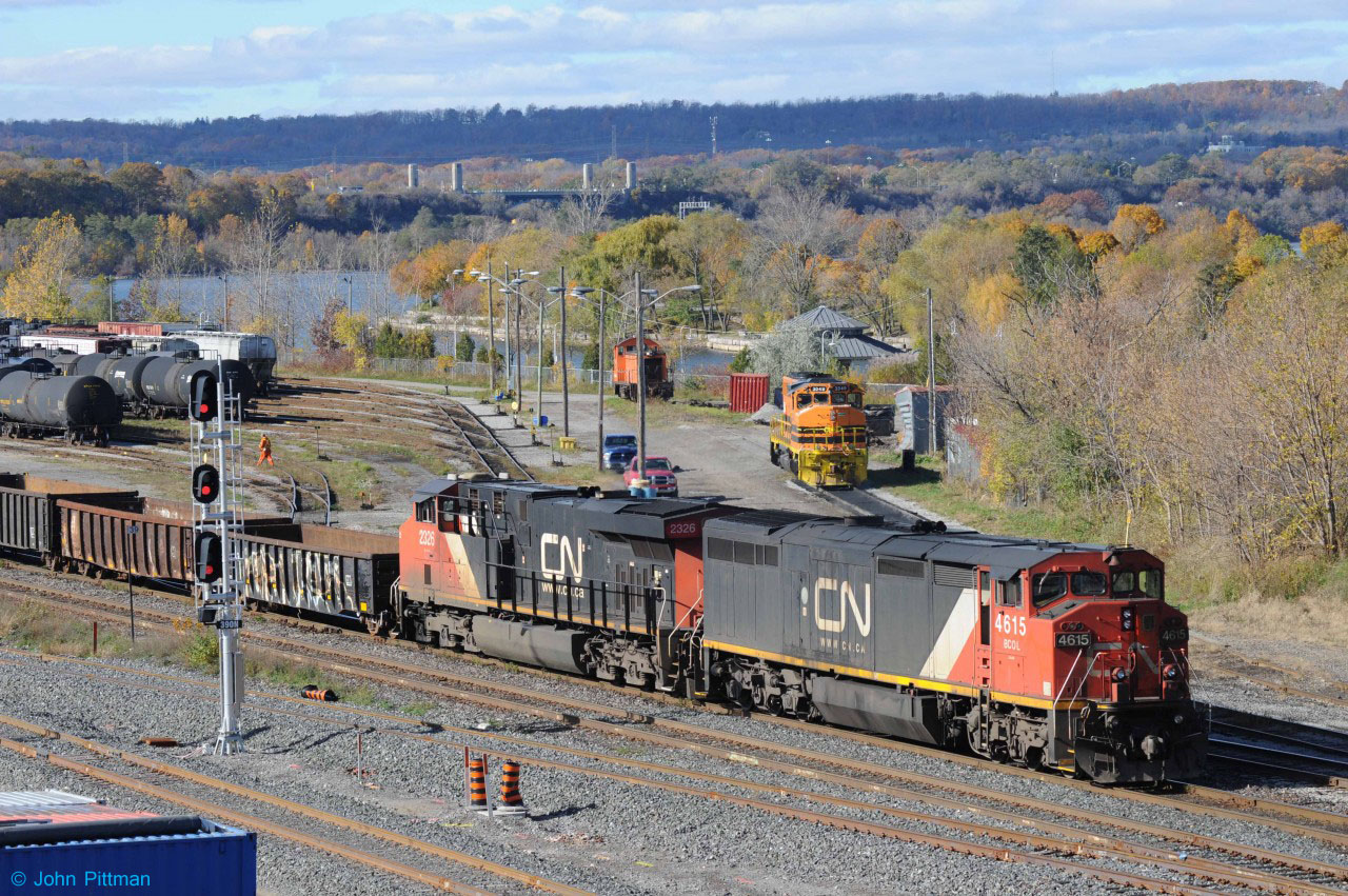 The view from Hamilton's Bay Street Bridge over CN/RailLink Stuart Street yard toward the High Level Bridge is a favorite of mine, in this case enhanced by the remaining autumn colours. Like me, many of you would have preferred BCOL 4615 in red, white and blue - though some of them need fresh paint. At 2:36PM on October 30 2015, Train 567 has completed its work at Hamilton Yard and awaits clearance for its return to the Grimsby sub. In the previous hour, the light engines had climbed the hill to Hamilton Junction and turned on the wye, keeping BCOL 4615 in the lead. From the radio, it sounded like they next backed into Aldershot yard to lift cars there before returning to Hamilton. Note the double set of ditch lights on 4615.  
Southern Ontario Railway unit RLHH 3049, ex-CN GP40-2W, is at rest, somewhat fogged by 4615's exhaust. On this day SOR 4003 was working the yard. 
Construction at the new Hamilton West Waterfront GO station and between Hamilton Jct and Bayview Jct has been providing radio warning of train movements in the area, but also some lengthy periods with no trains.