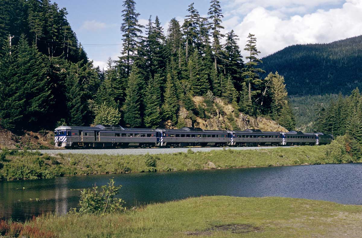 BC Rail daily passenger train passing a small lake just south of Whistler, BC in June 1993 with 6 RDC's.  This was one of the best rides in North America with premium Caribou service that included better seating and meals at your seat.  In early 1993 when I rode it, a round trip Caribou service ticket from North Vancouver to Lillooet was $97 compared to the regular fare of $52.  If both sides were on time, there was about a 3 hour layover in Lillooet.