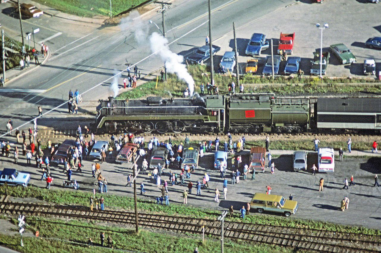 Even from the air, you can sense the excitement that 6060’s arrival generated!


It took a small army to confirm the date and location of this 35mm Kodachrome image.  Special thanks to Steve, Paul, Greg and Jim!


Steve:


Date is Sept 23, 1978.   That is from my records and log book.


Paul:


I'm going with Acton, westbound, must have been pretty early in the morning
as the shadows are very long.


Greg:


Those would be the shed tracks at the bottom of the frame, Wallace Street
coming in on the upper left.


Jim:


I think Paul's got it.  Looks to be Acton.