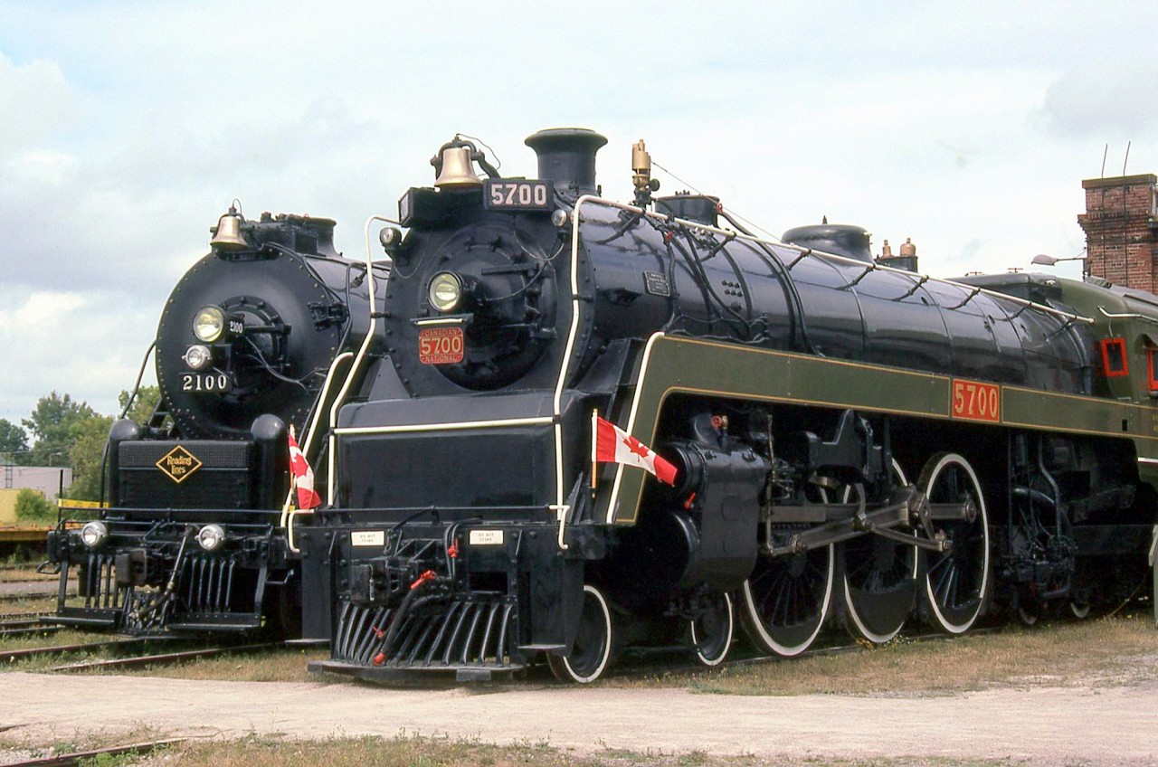 Big steam at St. Thomas: Canadian National 5700 and Reading 2100 pose next to each other on an Iron Horse day outside the former Michigan Central shop building at the Elgin County Railway Museum.CNR 5700 is a K5a-class 4-6-4 "Hudson" built for CN in November of 1930 by MLW. While CP accumulated 65 Hudson type steam locomotives, CN only rostered 5: 5700-5704. They were used in passenger service out of Spadina Roundhouse in downtown Toronto until eventual retirement at the end of the steam era. When retired, two were donated to museums: 5702 to the Canadian Railway Museum/Exporail in Delson QC, and 5703 (as 5700) to the National Museum of Science and Technology (NMST). CN had the intent to preserve the "class" unit of the group like Northerns 6200 and 6400 were, but the original 5700 was inadvertently scrapped, so 5703 was renumbered as 5700 when donated to the NMST in November 1961. In 1988, "5700" went to the Elgin County Railway Museum where it resides today.Reading 2100 is a Reading-built 4-8-4 Northern, at the time privately owned by Tom Payne and stored at ECRM with plans to put it into excursion service. It has since been sent back to the US, more details on 2100 can be found on the photo of it *here*.For a photo of sister CNR Hudson 5702 in passenger service: http://www.railpictures.ca/?attachment_id=14106