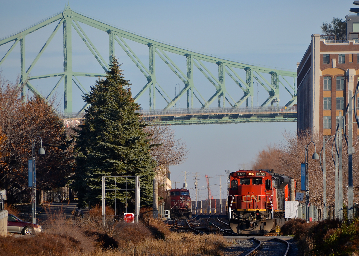 CN 149, with CP lurking. A CP GE is seen lurking to the left of CN 2103, which is leading CN 149. Both trains are on Port of Montreal Tracks.