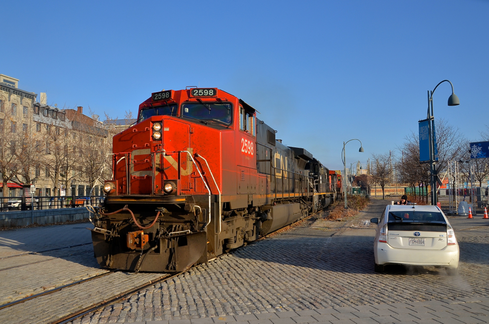 Past Port of Montreal security. CN 149 has just left Port of Montreal trackage and is on the CN Wharf Spur as it passes a crossing that is flagged by a Port of Montreal employee. The Port of Montreal security flags the many crossings in this busy and tourist-intensive area. Lashup is CN 2598, IC 1001 & CN 2631.