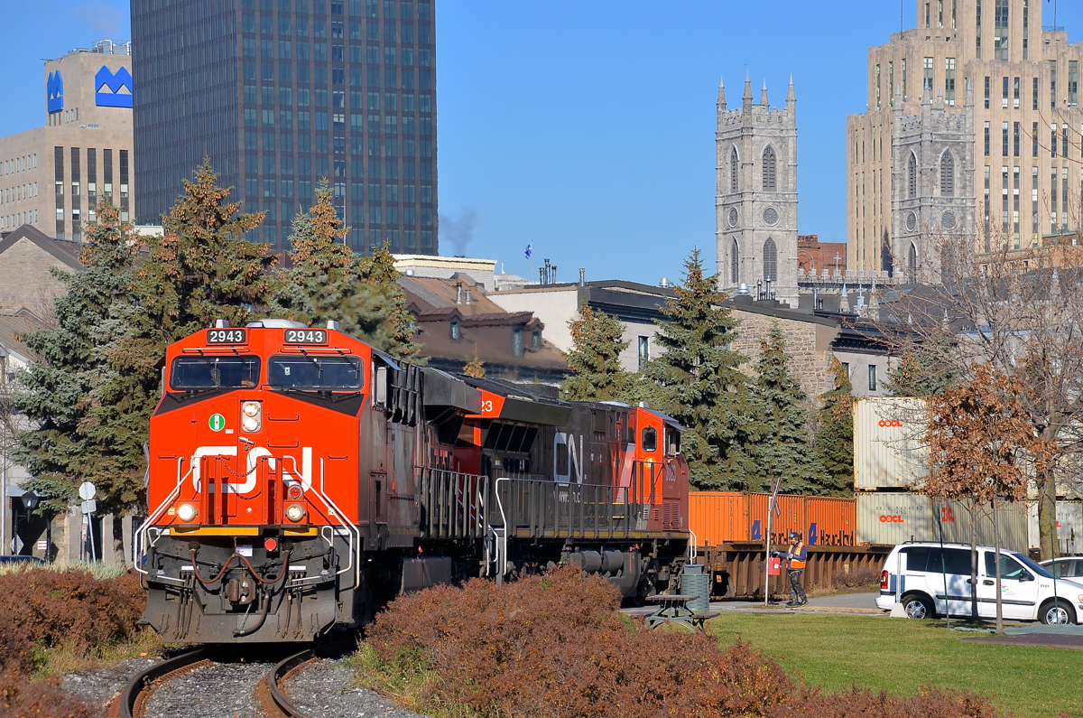 CN 149 curving. CN 2943 is in charge of CN 149 as it rounds a curve in the Port of Montreal, with CN 3023 trailing. In a few seconds the head end will cross the Lachine canal on a sunny fall morning. At right is a Port of Montreal employee flagging this crossing.