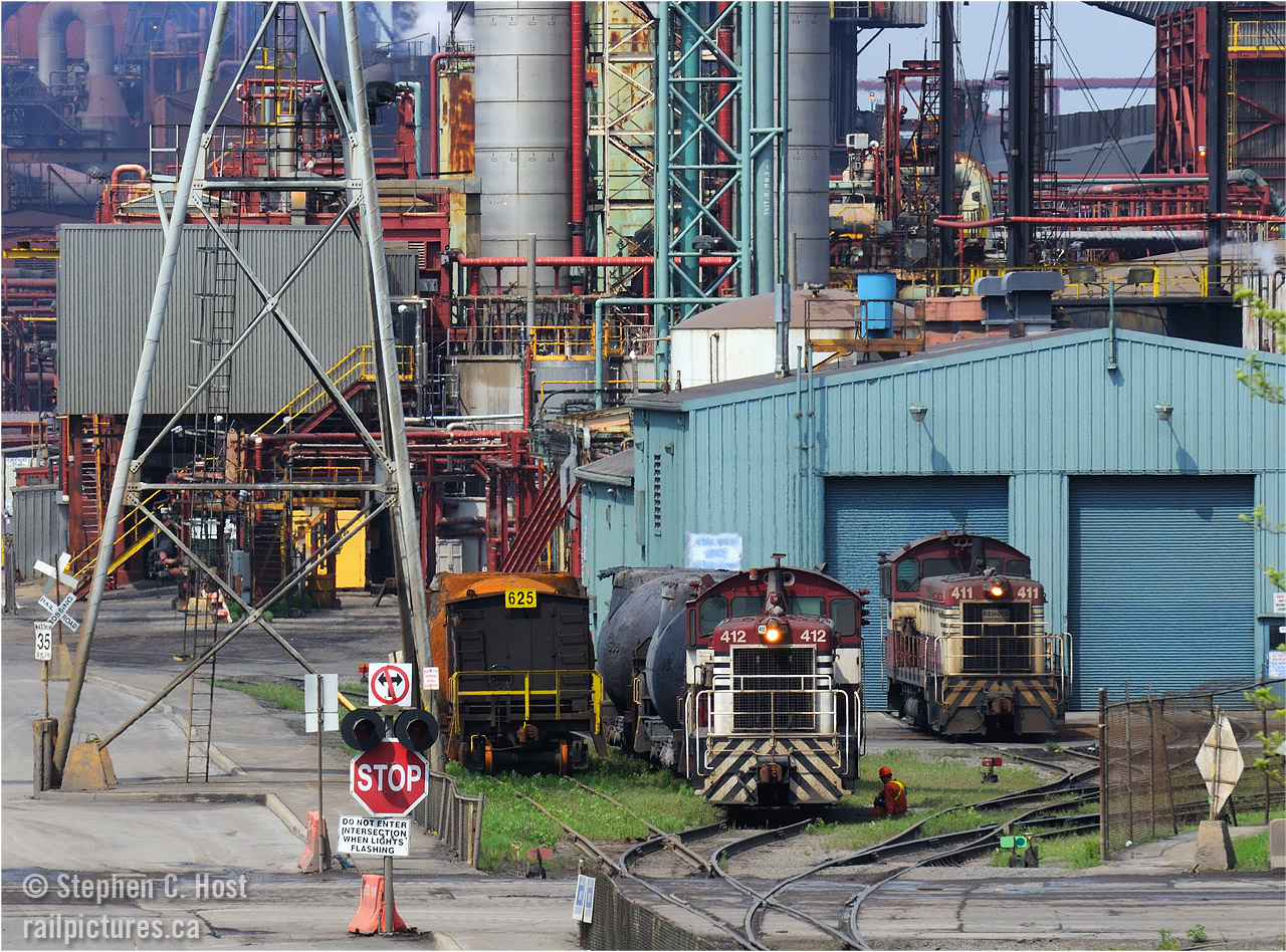 In the industrial heartland of Hamilton a pair of consecutive EMD SW8's Dofasco 411 and 412 sit side by side at the railway's main shop while a transportation dept employee has lunch on the 'grass'. 412 has a Bottle train  and this is a very rare sight - the bottle trains work deep in the plant and are rarely visible from public property. 411 is at the shop proper. To the left of the bottle train is NEW bottle car 625 recently delivered after heading for refurbishment. Recently, Gensets have started making inroads at the former Dofasco and the SW8's days may be numbered. As alluded, this  photo was taken from Public property.