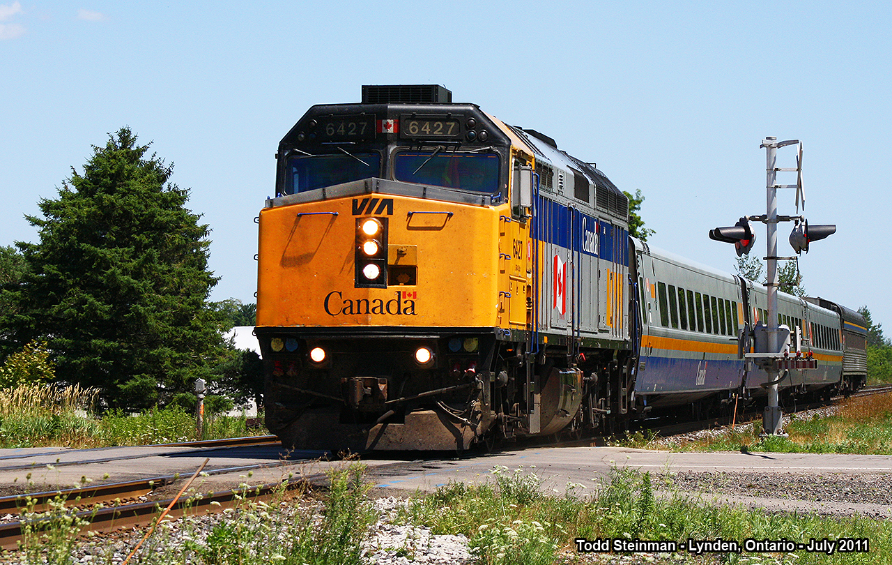 VIA 6427 flies across Main Street in Lynden, leading it's four car consist to it's next station stop at Brantford. Note how this engine was modified...most distinguishing is the addition of the third headlight. My first sighting of this paint scheme on 6427 was 1989 - I departed a train at Napanee and saw not only was the new motive power for VIA Rail at that time, but this paint scheme as well. Although this paint scheme was modified through the years, 6427 was finally repainted to the current design. I didn't realize it at the time, but I photographed 6427 only this past weekend (Oct. 31st 2015) in Port Hope:  http://www.railpictures.ca/?attachment_id=21408#sthash.c9mx3wOl.dpuf A transformation indeed.