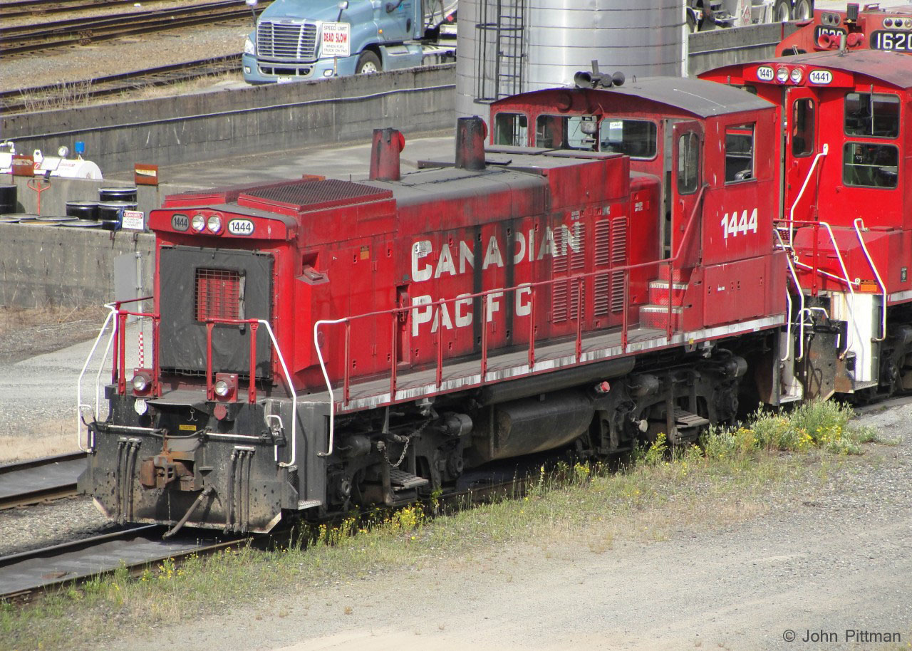 MP15 CP 1444 is at rest beside the fuel storage area on the east side of CP's Port Coquitlam BC diesel shop.
A fuel tanker is on the pad, so the speed limit is Dead Slow, according to the sign. 
Vantage point was the sidewalk of the Coast Meridian Overpass (bridge across the width of Port Coquitlam yard). The Sony compact camera that I used has a lens small enough to fit through the tight chain link mesh (about one inch pitch) that runs right across the bridge.