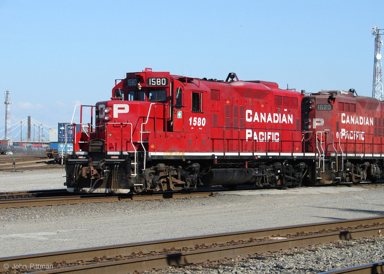 GP9u CP 1580 in clean paint is in its last 6 months of operation, as it switches railcars at Port Coquitlam Yard paired with CP 1620. 
Looks like the original bell was replaced by that device between the (former) dynamic brake bulges. From the original bell bracket someone has hung a teddy bear. 
The bridge in the distance is the Coast Meridian Overpass, opened March 2010. Its sidewalk provides some nice views of CP locomotives on the east side of the diesel shop in the morning, as well as yard activity - but it has inch pitch chainlink, so a good small camera is your best bet there.