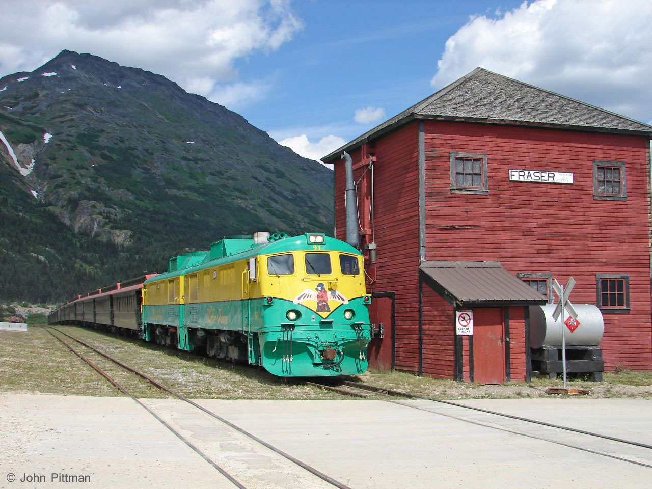 GE shovelnose unit WPY 91 and WPY 97 are coupled onto their train at Fraser BC for the trip south to Skagway. Departure is just minutes away.
For a number of years the water tank in the lineside building was out of service - current status unknown - but Bernard Lake is nearby. 
While at Fraser I heard the howl of another re-engined White Pass Route train approaching and waited for it. The sound faded away, that train was never seen.   Much later I discovered that there is a turning loop a short way south of Fraser BC, just out of sight.  On busy days, when more trains arrive at White Pass Summit than there is track to hold them, one or more continue to this loop to turn.  The loop is also near essential for their steam engine hauled trains.  Unfortunately Google maps only shows the south end of the WP&YR.